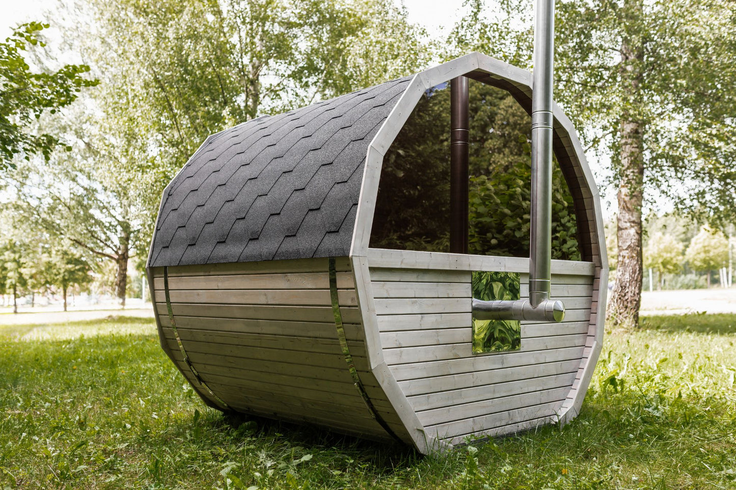 Runde Außensauna aus hochwertigem Fichten- oder Thermoholz, geeignet für 4–Personen. Mit Lindenholz-Bänken, Bitumenschindeln-Dach, Sicherheitsglas-Türen und Harvia-Beleuchtung.Außenansicht