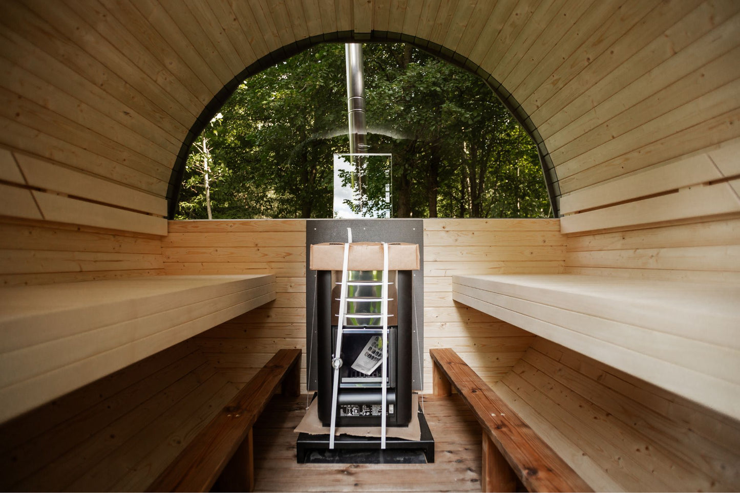 Runde Außensauna aus hochwertigem Fichten- oder Thermoholz, geeignet für 4–Personen. Mit Lindenholz-Bänken, Bitumenschindeln-Dach, Sicherheitsglas-Türen und Harvia-Beleuchtung.Bild innen