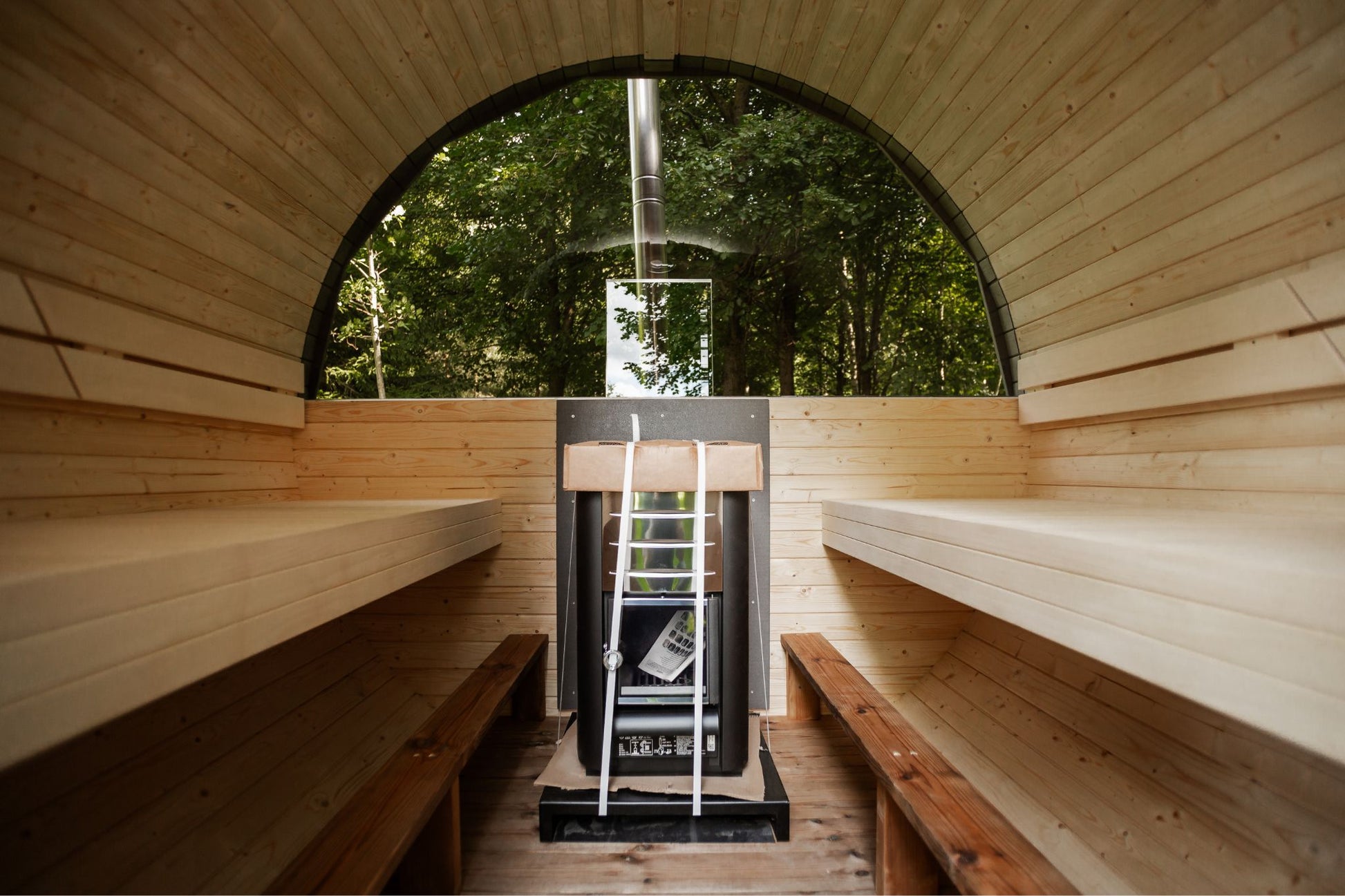 Runde Außensauna aus hochwertigem Fichten- oder Thermoholz, geeignet für 4–Personen. Mit Lindenholz-Bänken, Bitumenschindeln-Dach, Sicherheitsglas-Türen und Harvia-Beleuchtung.Bild innen