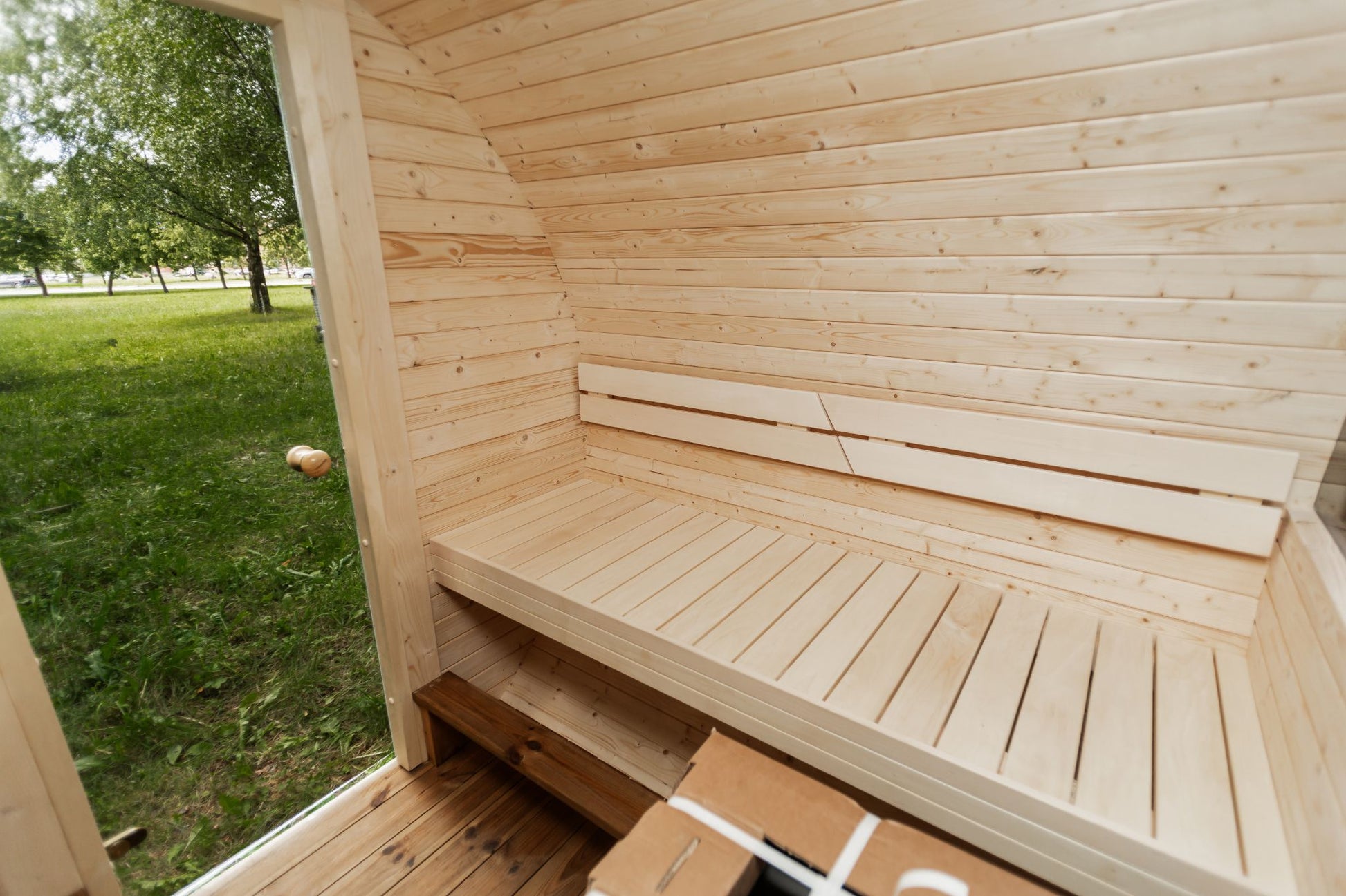 Runde Außensauna aus hochwertigem Fichten- oder Thermoholz, geeignet für 4–Personen. Mit Lindenholz-Bänken, Bitumenschindeln-Dach, Sicherheitsglas-Türen und Harvia-Beleuchtung.Bild innen
