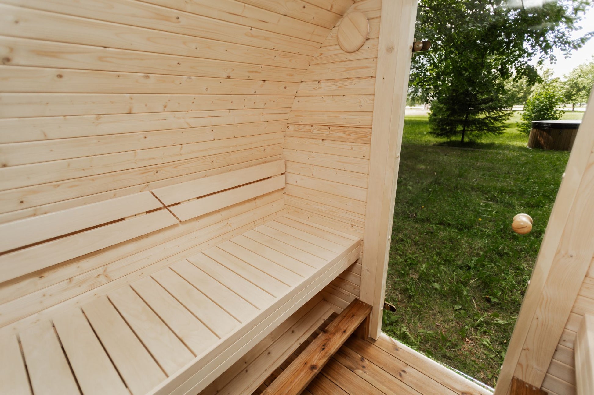 Runde Außensauna aus hochwertigem Fichten- oder Thermoholz, geeignet für 4–Personen. Mit Lindenholz-Bänken, Bitumenschindeln-Dach, Sicherheitsglas-Türen und Harvia-Beleuchtung.Bild innen