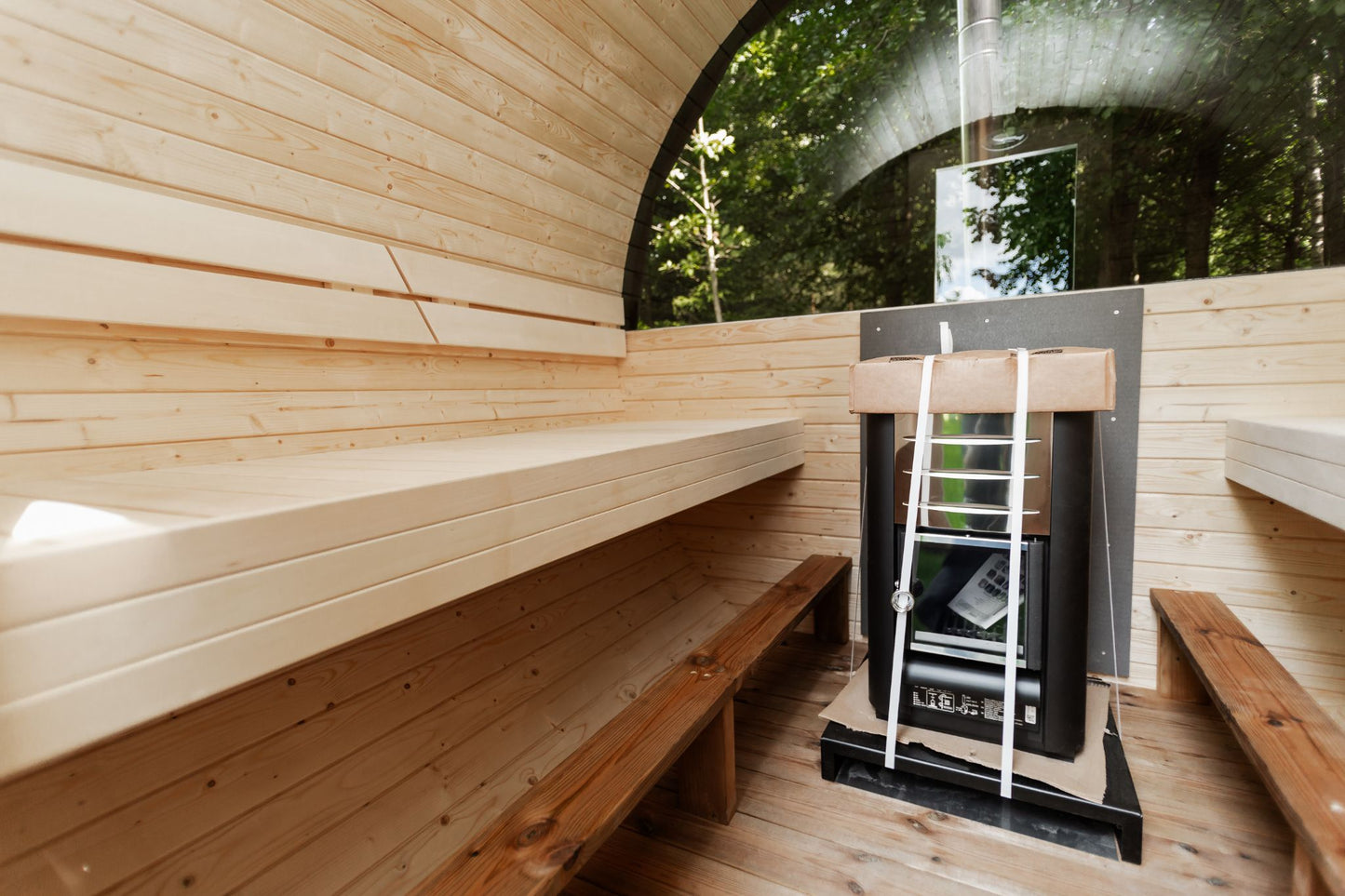 Runde Außensauna aus hochwertigem Fichten- oder Thermoholz, geeignet für 4–Personen. Mit Lindenholz-Bänken, Bitumenschindeln-Dach, Sicherheitsglas-Türen und Harvia-Beleuchtung.Bild innen