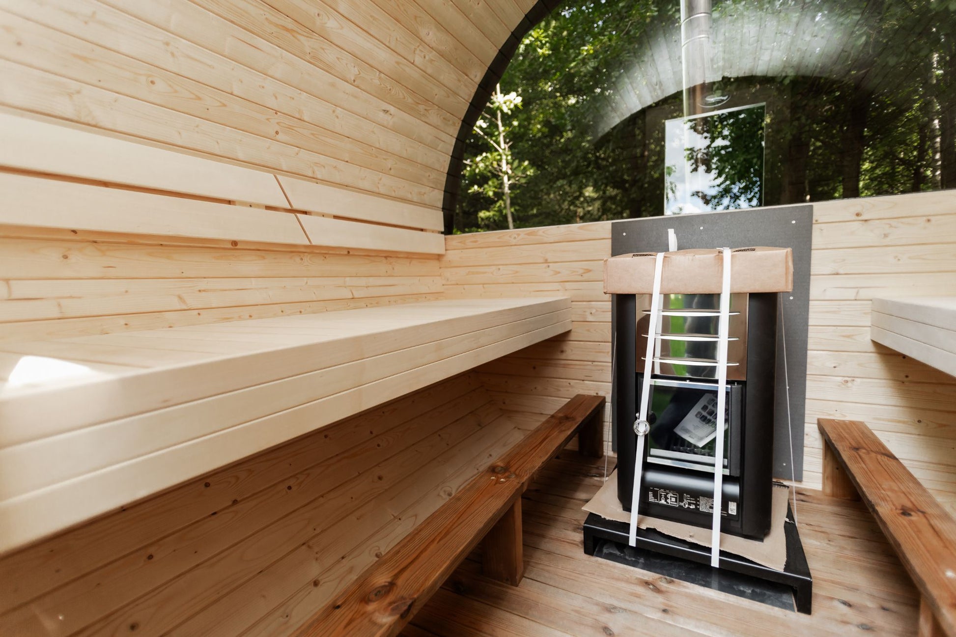 Runde Außensauna aus hochwertigem Fichten- oder Thermoholz, geeignet für 4–Personen. Mit Lindenholz-Bänken, Bitumenschindeln-Dach, Sicherheitsglas-Türen und Harvia-Beleuchtung.Bild innen